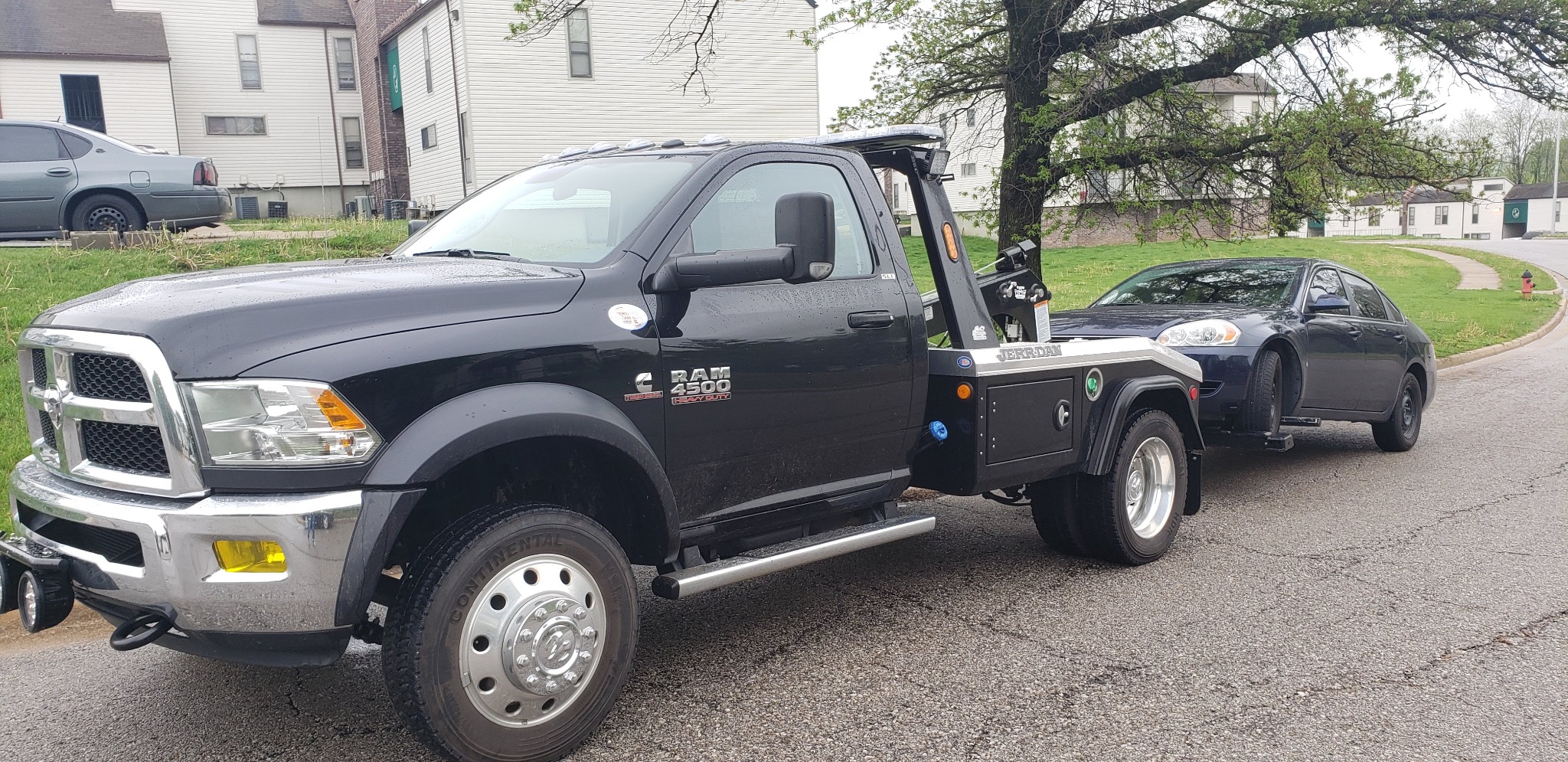 Black self-loading recovery truck positioned with a dark passenger vehicle on a street in Louisburg Kansas