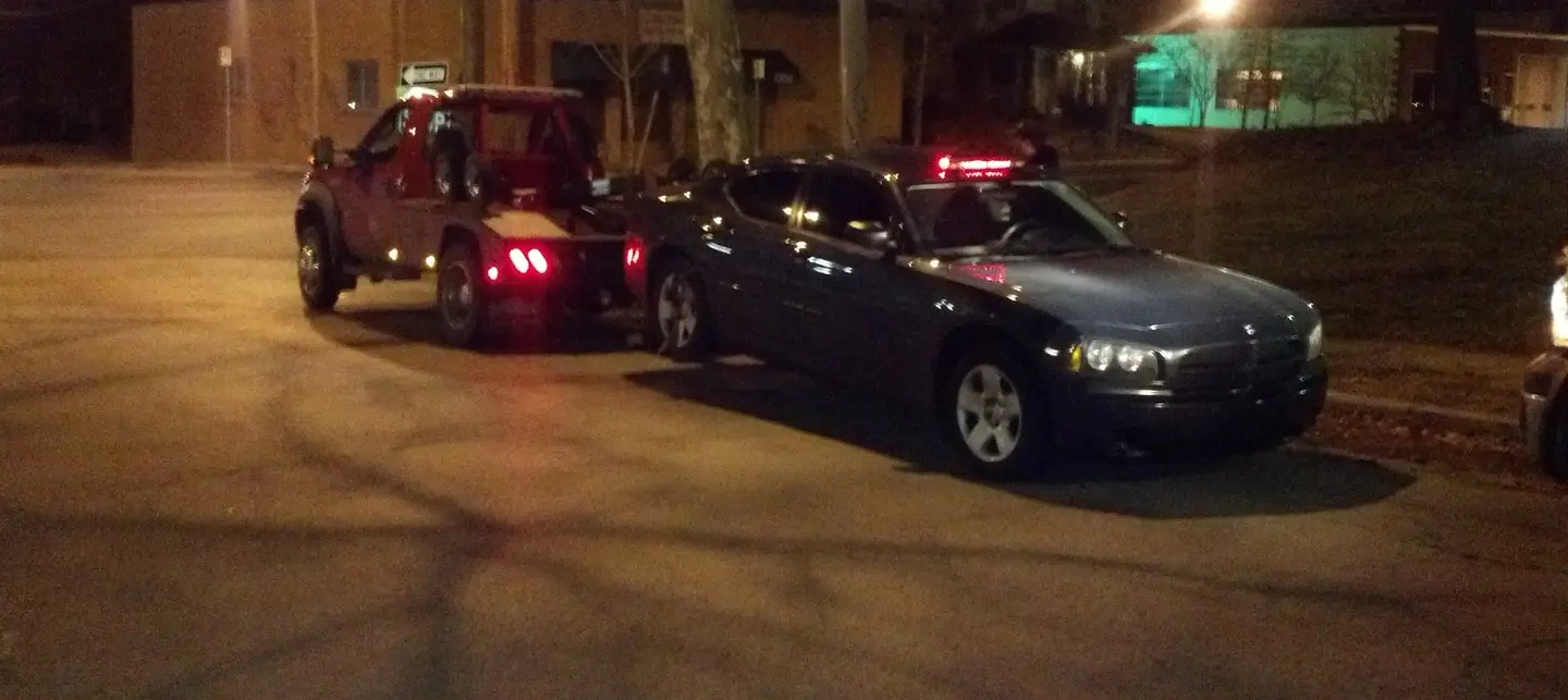 LRS wheel-lift tow truck positioned with a dark passenger car during a nighttime recovery in Mission Kansas